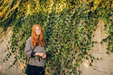 Dışında poz, onay ceket ve siyah etek giyen sevimli küçük kızıl saçlı kız portresi 