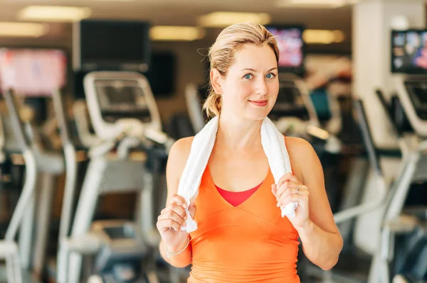 Happy and healthy woman in sport gym, holding white towel