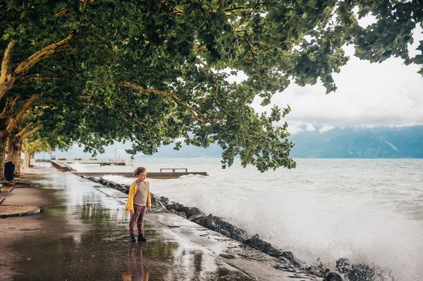 可爱的小男孩在一个风很大的日子在湖边玩耍 看着海浪 穿着黄色雨衣 在瑞士洛桑日内瓦湖拍摄的图片 — 图库照片