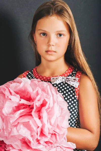 スタジオ撮影水玉を身に着けているかわいい女の子のドレス 黒い背景にポーズをとって ピンク色の巨大な紙の花を保持 — ストック写真