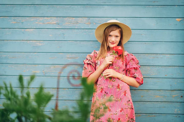 夏の赤のストライプ ドレス 麦わら帽子をかぶって バラの花を持って 明るい青い木製の背景にポーズかわいい女の子の肖像画 — ストック写真