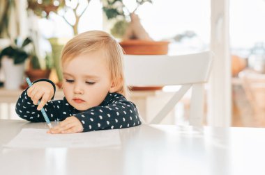 Masa başında oturan sevimli bebek kız Pancils ile çizim