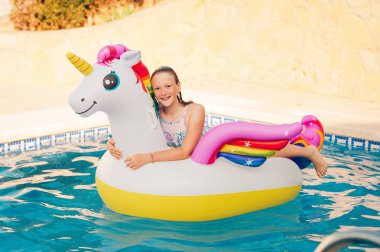 Havuzda oynarken, şişme renkli tek boynuzlu at üzerinde rahatlatıcı mutlu genç kız