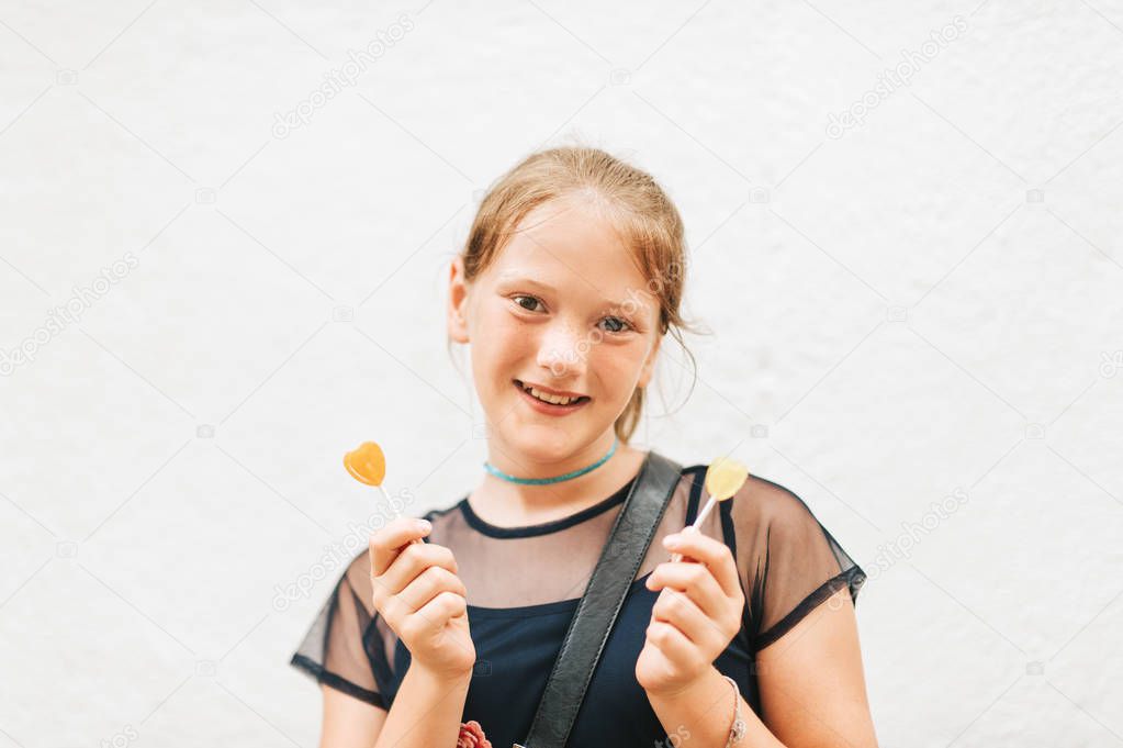 Outdoor portrait of cute kid girl holding heart shaped lollipop candies