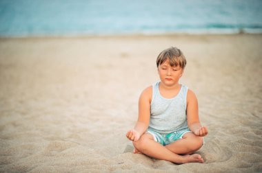 Sevimli küçük çocuk güzel güneş ışığı altında sahilde meditasyon