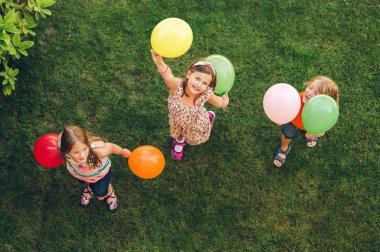 Mutlu üç küçük renkli balonlar ile açık havada, üstten görünüm oynayan çocuklar