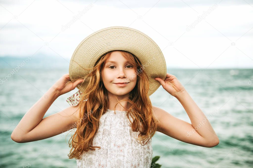 Outdoor portrait of pretty young kid girl with red hair, wearing big hat, family vacation with children by the sea