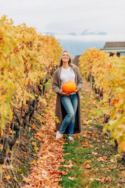 Sonbahar turuncu kabak holding, örme kahverengi longline hırka giymiş, altın üzüm bağları poz sarışın kıvırcık saçlı güzel kadın portresi