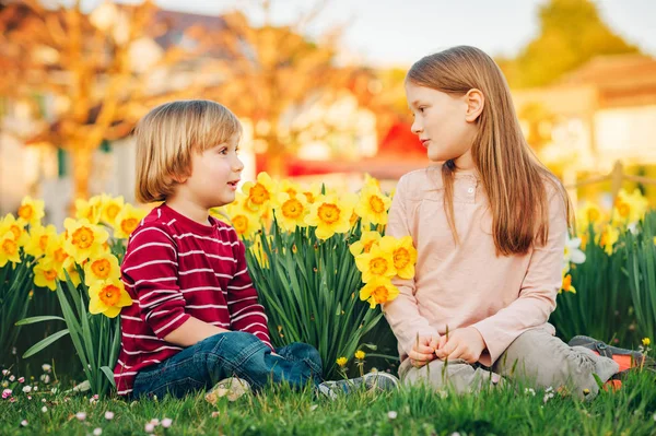 两个可爱的孩子 小男孩和他的大姐 在阳光下黄色水仙花之间的公园里玩耍 — 图库照片
