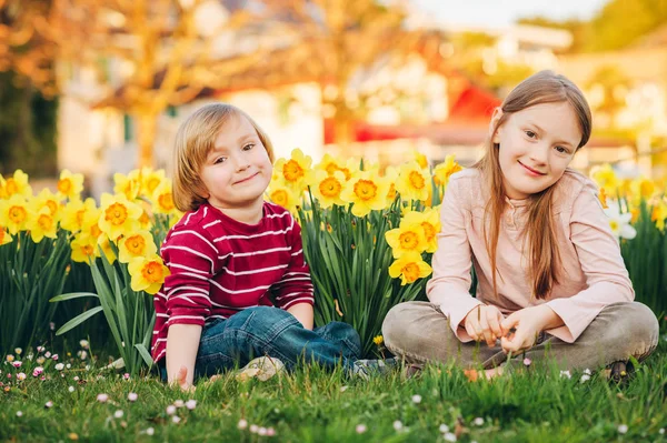 两个可爱的孩子 小男孩和他的大姐 在阳光下黄色水仙花之间的公园里玩耍 — 图库照片