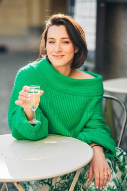 Koyu saçlı güzel bir kadının açık hava moda portresi, yeşil pullover giyiyor, sokak kafede poz