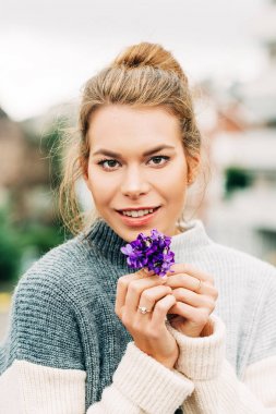 Sıcak gri pullover giyen güzel genç kadının Bahar portre, Yünlü Mavi Menekşe küçük bir buket tutan (Viola sororia)