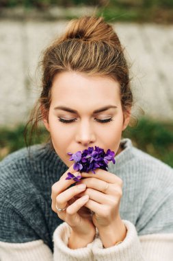 Sıcak gri pullover giyen güzel genç kadının Bahar portre, Yünlü Mavi Menekşe küçük bir buket tutan (Viola sororia)