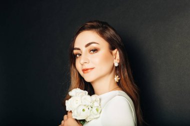 Stüdyo uzun parlak saçlı güzel genç kadının portresi kadar yakın, profesyonel makyaj, beyaz elbise giyen, buttercup çiçekler tutan