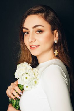 Stüdyo uzun parlak saçlı güzel genç kadının portresi kadar yakın, profesyonel makyaj, beyaz elbise giyen, buttercup çiçekler tutan