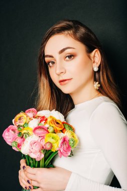 Stüdyo uzun parlak saçlı güzel genç kadının portresi kadar yakın, profesyonel makyaj, beyaz elbise giyen, renkli buttercup çiçekler tutan