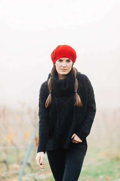 户外肖像美丽的年轻女子在雾背景上摆姿势穿着黑色拉扯和红色贝雷贝 — 图库照片