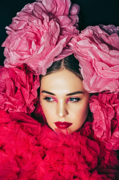 Close up portrait of beautiful young model with bright fashion makeup, wearing big pink fluffy collar, covered with decorative paper flowers