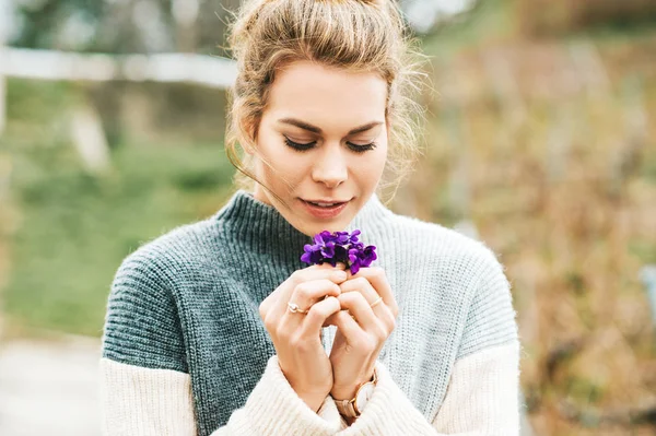 Sıcak gri pullover giyen güzel genç kadının Bahar portre, Yünlü Mavi Menekşe küçük bir buket tutan (Viola sororia)