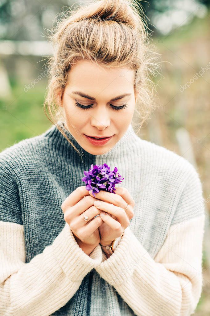 Spring portrait of pretty young woman wearing warm grey pullover, holding small bouquet of Woolly Blue Violet (Viola sororia)