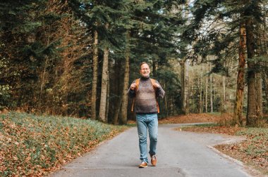 Yakışıklı orta yaş adam ormanda yürüyüş, pullover, sırt çantası ve gözlük giyiyor