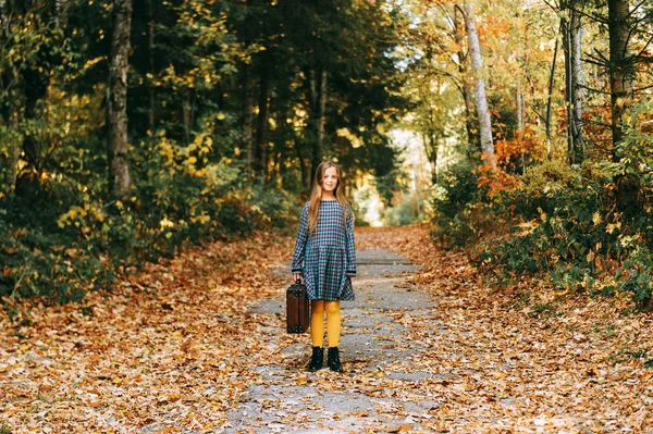 古いヴィンテージスーツケースを持つかわいい若い女の子の秋の肖像画 森の中で屋外でポーズをとる子供モデル チェック柄のドレスと黄色のタイツを着て — ストック写真
