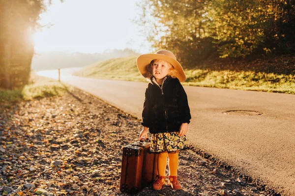 古いヴィンテージスーツケースを保持し 大きな帽子 黒いコートと黄色のタイツを身に着けている愛らしいかわいい幼児の女の子の屋外の肖像画 — ストック写真