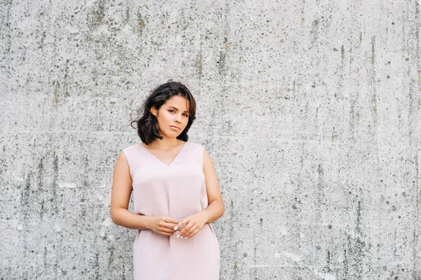 Urban fashion portrait of beautiful young woman posing on gray wall background