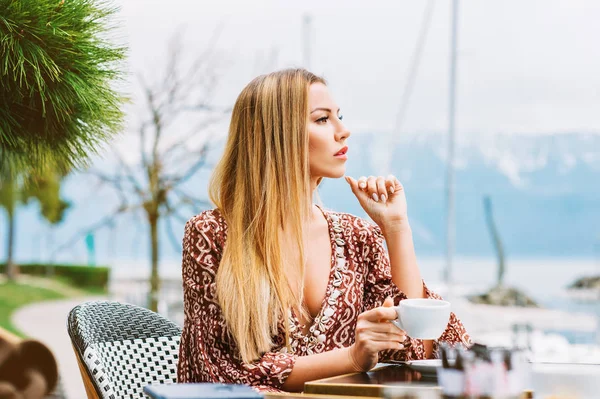 Outdoor portrait of beautiful woman resting in cafe with cup of coffee