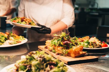 Restorandaki mutfak masasında yemek siparişleri. Üstüne taze farklı türde yeşil salata ile Puf böreği tabanı