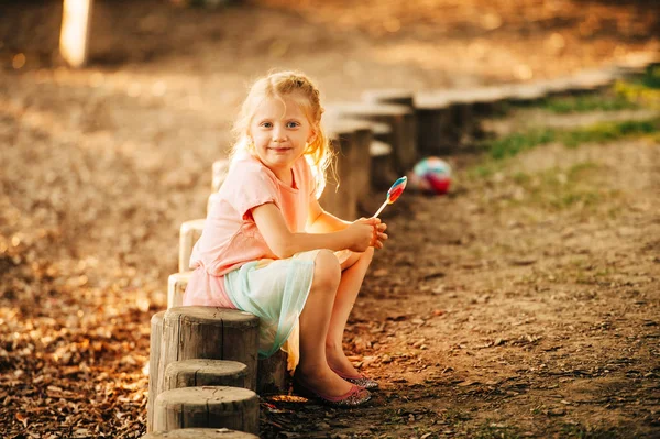 户外肖像有趣的小女孩与棒棒糖糖果在阳光明媚的公园 黄金时间图像 — 图库照片