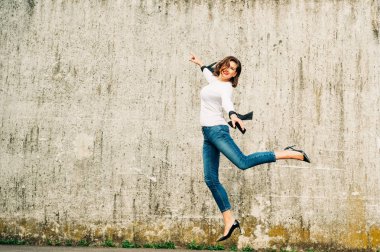 Şehrin tepesinde zıplayan mutlu genç bir kadının açık hava portresi.