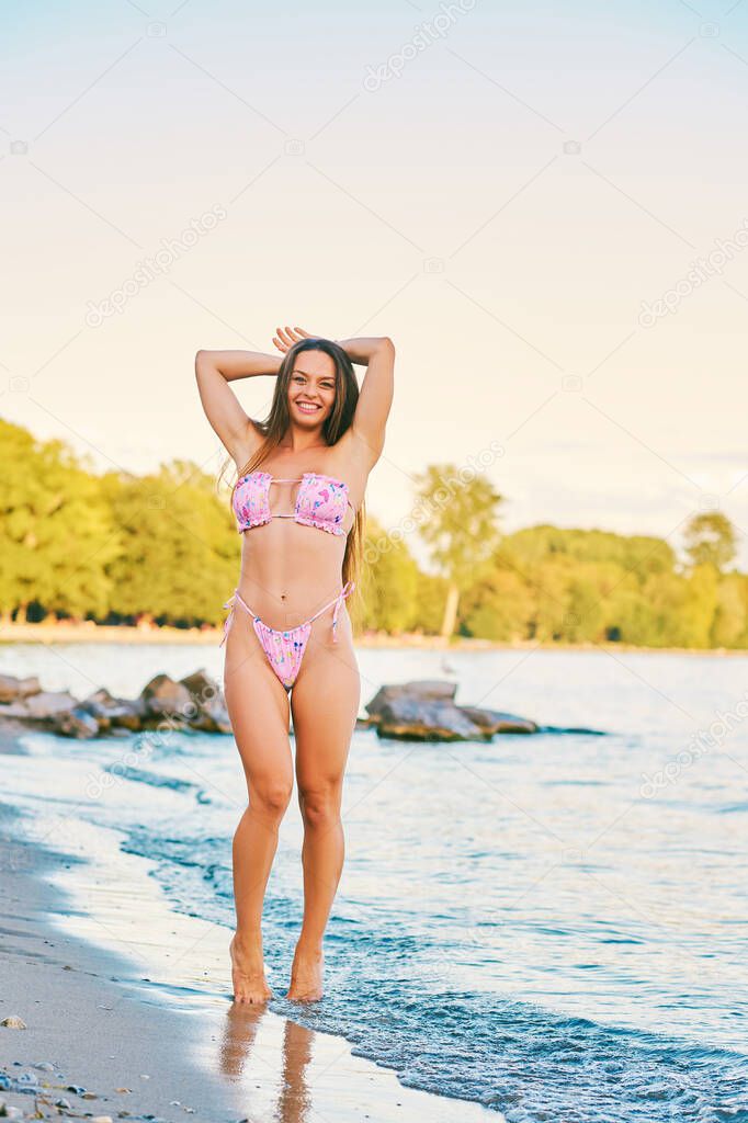 Outdoor portrait of beautiful young woman having fun by the lake, wearing pink bikini