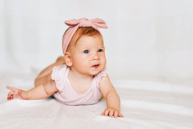 Sevimli kızıl saçlı bebeğin portresi göbeğinde, beyaz arka planda, pembe bir vücut ve saç bandı takıyor.