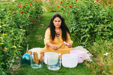 Kadın kristal kaselerde müzik çalıyor, güzel yeşil bahçede dinleniyor.