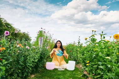 Kadın kristal kaselerde müzik çalıyor, güzel yeşil bahçede dinleniyor.