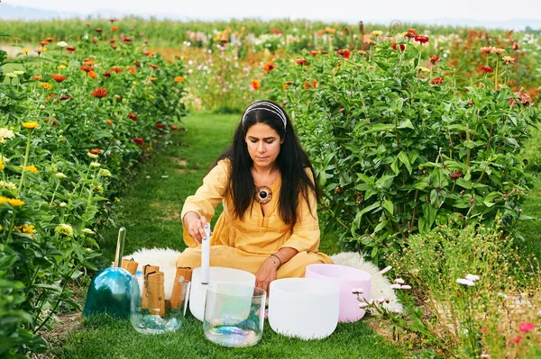 Kadın kristal kaselerde müzik çalıyor, güzel yeşil bahçede dinleniyor.