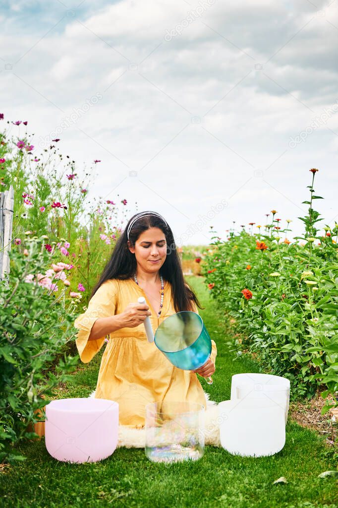 Woman playing music on crystal singing bowls, relaxing in beautiful green garden