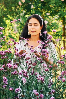 Açık havada, güneşli bahçede orta yaşlı bir kadının portresi verbena çiçeklerinin kokusundan zevk alıyor.