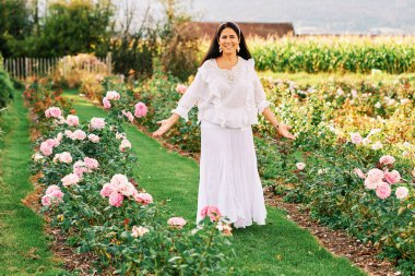 Güzel gül bahçesinde güzel bir gün geçiren beyaz elbiseli bir kadın.