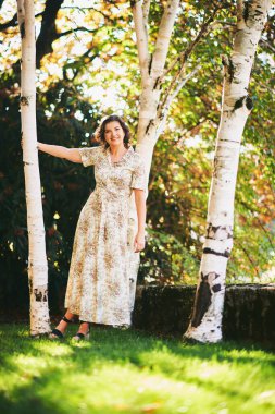 Huş ağacının yanında poz veren mutlu genç kadının açık hava portresi.