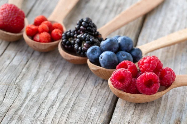 Ripe berries in wooden spoons — Stock Photo, Image