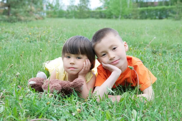孩子们躺在公园的草地上玩得很开心 小女孩和男孩笑着放松 泰迪熊玩具一起 — 图库照片