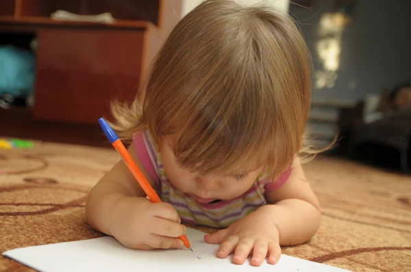 Baby girl learning to write and paint in home environment lying on carpet