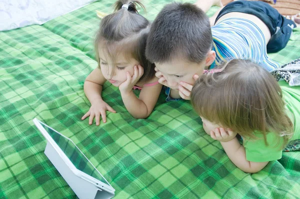 三个孩子躺在家里的床上看平板电脑 孩子们的时间花 孩子们使用垫电脑 — 图库照片