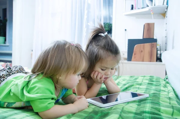 小女孩们躺在家里的床上看着垫子 孩子们的时间花 使用平板电脑的孩子 — 图库照片