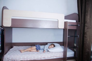 Çocuk odası ranza yatak. küçük kız yatakta yatarken tek başına. Çikolata gölge beyaz duvarlı iç. Çocuk odaları için kahverengi mobilya