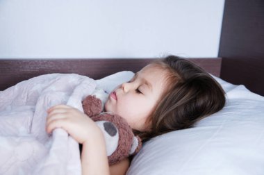 küçük kızlar yatakta yatarken uyuyor. uyku düzeni iç yaşam tarzı. şirin bebek çocuk ayı ile