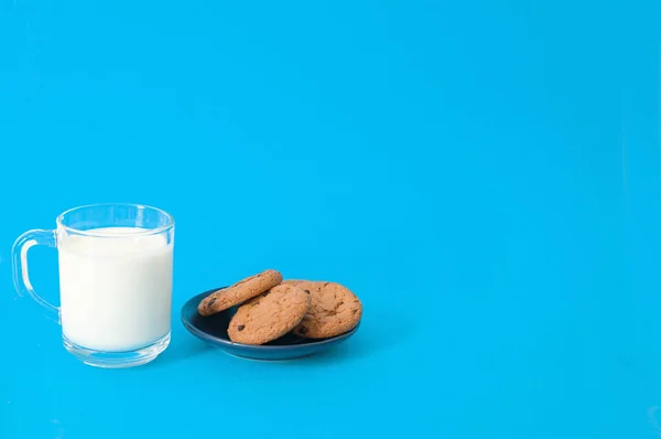 青色の背景にプレートとミルクのガラスのクッキー チョコレートの作品とオートミールクッキー — ストック写真