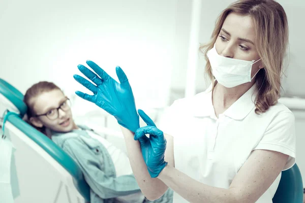 Attentive young dentist putting on blue gloves — Stock Photo, Image